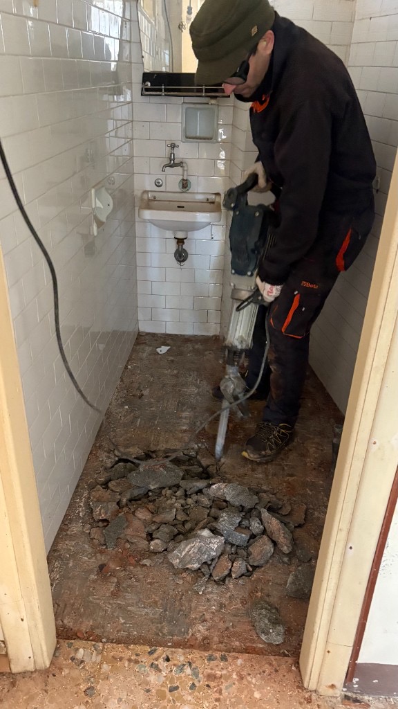 Demolizione del pavimento in un bagno piastrellato con martello pneumatico, occhiali e guanti