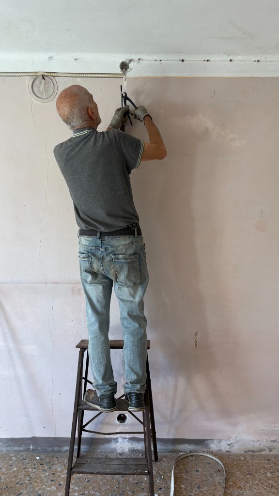Volontario su una scala mentre lavora a un impianto su una parete interna durante il cantiere